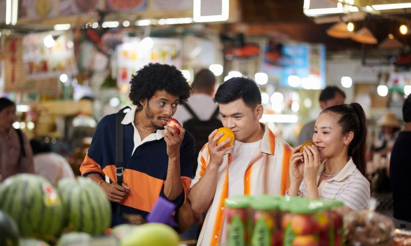 A group of friends at a market inspecting produce and enjoying the smells as a means of mindful eating for healthier life choices around diabetes management