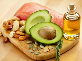 A wooden board with healthy fats like avocado, olive oil, and nuts for a healthy diet.