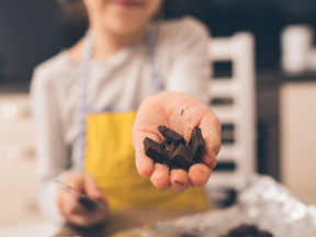 A person cutting up dark chocolate and offering it towards the camera