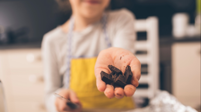A person cutting up dark chocolate and offering it towards the camera