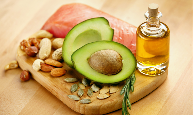 A wooden board with healthy fats like avocado, olive oil, and nuts for a healthy diet.